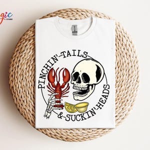 K&ouml;nnte beinhalten: Wei&szlig;es T-Shirt mit einer schwarz-wei&szlig;en Illustration eines Sch&auml;dels und eines Hummers mit dem Text "Pinchin' Tails & Suckin' Heads".