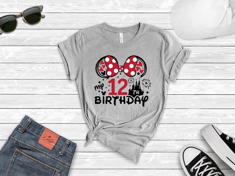 Pu&ograve; includere: Maglietta grigia con un fiocco di Minnie Mouse rosso e bianco, un castello, fuochi d'artificio e il testo "my 12th birthday".