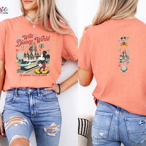 May include: Coral t-shirt with a Walt Disney World design on the front and back. The front features a castle, train, Mickey Mouse, and the text "Walt Disney World" and "The Happiest Place on Earth." The back has a vertical design with Mickey Mouse, a castle, and a globe.