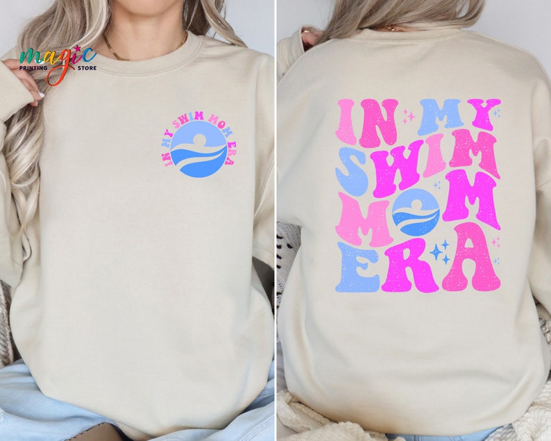 May include: A cream-coloured sweatshirt with the text "In My Swim Mom Era" in pink, blue and white letters. The text is in a retro font style with stars and a swimmer graphic.