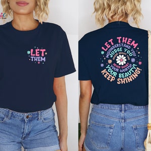 May include: A navy blue t-shirt with the text "Let them misunderstand you, judge you, gossip about you, never doubt your worth, your beauty, keep shining!" in a circle with a pink daisy in the center. The text is in a pink, blue, and green font.