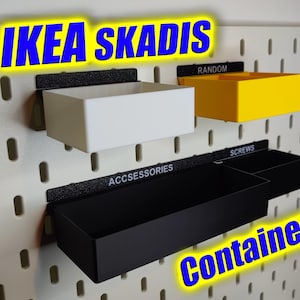 May include: Three black, white and yellow plastic storage containers with labels that say "Accessories", "Screws" and "Random". The containers are mounted on a white pegboard wall. The text "IKEA SKADIS Containers" is written in blue and yellow letters across the top of the image.