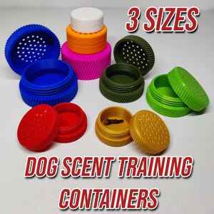 May include: A selection of brightly coloured dog scent training containers. The containers are in blue, red, green, yellow, pink, and orange. The image includes the text "3 SIZES" and "DOG SCENT TRAINING CONTAINERS".