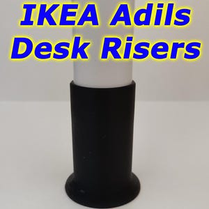 May include: Black plastic desk riser for IKEA ADILS table legs. The riser is cylindrical with a flared base.