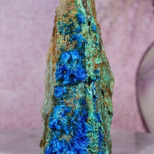 May include: A vertical mineral specimen featuring a rough, textured surface with vibrant blue crystalline clusters embedded within a matrix of earthy brown and bright green mineral deposits, standing upright with a pointed, jagged top edge.