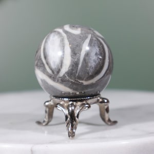 May include: A gray and white striped sphere on a silver stand. The sphere is made of polished stone and has a smooth, glossy finish.
