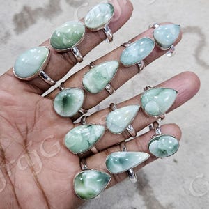 May include: A collection of silver rings with green gemstone teardrop settings. The rings are displayed on a hand.