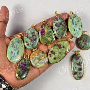 Peut inclure: Une collection de pendentifs en pierres précieuses avec des montures dorées. Les pendentifs présentent un motif tacheté vert et rose. Les pendentifs sont de formes variées, dont ovales, en forme de goutte et ronds. Les pierres précieuses sont maintenues par un métal doré.