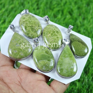 Può includere: Sei ciondoli in pietra preziosa verde con montature in argento. I ciondoli sono di varie forme, tra cui ovale e a goccia. I ciondoli sono esposti su una carta bianca con il testo "gajraj gems".