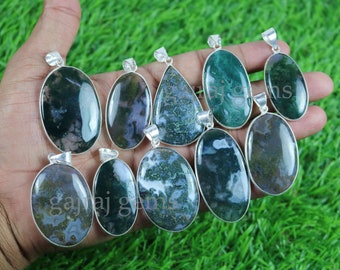 May include: A collection of moss agate pendants with silver-colored settings. The pendants vary in shape, including oval and teardrop, and display green and white patterns. The pendants are displayed against a green background.