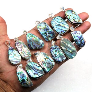 Op de afbeelding: Een verzameling van 12 iriserende abalone-schelp hangers met zilveren beugels. De hangers zijn in verschillende vormen en maten, met een mix van blauwe, groene en paarse tinten.