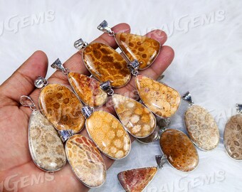 Può includere: Una collezione di pendenti in corallo di varie forme, tra cui ovali, a goccia e irregolari. I pendenti presentano un motivo corallino naturale e strutturato in tonalità beige, arancione e marrone, incastonati in metallo argentato. I pendenti sono esposti su una superficie bianca.