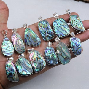 May include: A collection of 12 silver pendants featuring iridescent abalone shell in various shapes and sizes. The pendants are displayed on a hand.