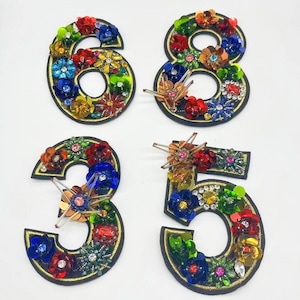 Könnte beinhalten: Vier bunte, bestickte Zahlen, 3, 5, 6 und 8, mit Pailletten und Perlen. Die Zahlen befinden sich auf einem weißen Hintergrund.