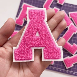 May include: Pink felt letter A with a white outline. The letter is thick and has a fuzzy texture.