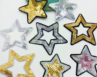 May include: Assortment of 10 gold, silver, and pink star-shaped iron-on patches. The stars are decorated with sequins and have a variety of designs.