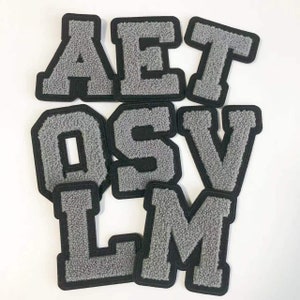 May include: A set of grey felt letters with black outlines. The letters are A, E, T, O, S, V, L, and M.
