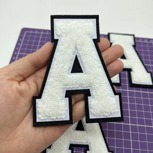 May include: White felt letter A with a black outline. The letter is thick and has a varsity style.