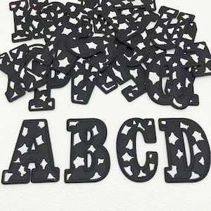 May include: Black and white fabric alphabet letters with a cow print design. The letters are in various sizes and fonts, with the letters "ABCD" in a larger size at the bottom.