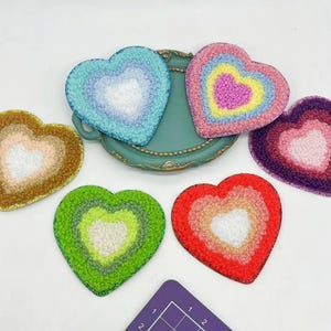Op de afbeelding: Zes kleurrijke hartvormige viltpatches met een gelaagd ontwerp. Elke patch heeft een andere kleurencombinatie, waaronder roze, blauw, groen, paars en oranje.