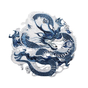 May include: A blue and white embroidered patch featuring a dragon with intricate details. The dragon is curled around itself, with its head facing the viewer. The patch has a white background with a blue dragon design. The dragon's scales are visible, and its eyes are black. The patch has a circle with the Chinese character "夢" (dream) in the center.