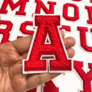 May include: Red felt letter patches in the alphabet, including the letters A, M, N, O, R, S, T, U, and Y. The letters are outlined in white and have a fuzzy texture.