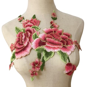 Puede incluir: Aplicación floral bordada con grandes flores rosas y rojas en capas, hojas verdes y ribete dorado. Diseñado para coser sobre tela, agregando un toque decorativo a prendas o manualidades.