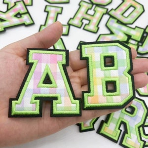 Könnte beinhalten: Buchstaben A und B in einem grün-weißen Gingham-Muster mit grünem Umriss und schwarzem Hintergrund.