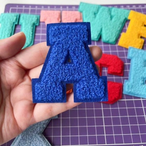 Może przedstawiać: Niebieska litera A z filcu z białym obramowaniem. Litera jest naszywką i ma puszystą fakturę.
