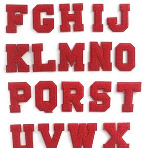 Op de afbeelding: Een set van 26 rode vilt letter patches, elke letter van het alfabet is individueel uitgesneden. De letters zijn in hoofdletters en hebben een licht verhoogd, getextureerd oppervlak.
