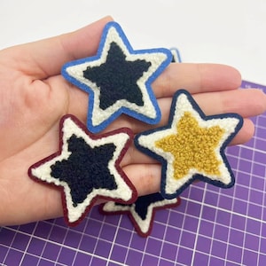Peut inclure: Quatre patchs en forme d'étoile en feutre avec des contours blancs. Les étoiles sont noires, rouges, bleues et jaunes.