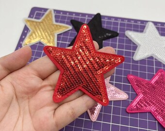 May include: Assortment of five star-shaped iron-on patches. The patches are made of sequins and come in red, pink, gold, black, and white.