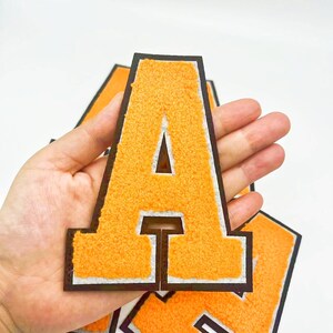 May include: Orange felt letter A with a white outline and black border. The letter is thick and has a fuzzy texture.