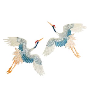 Op de afbeelding: Twee geborduurde witte en blauwe kraanvogelpatches met rode snavels en oranje poten. De kraanvogels zijn in vlucht met uitgespreide vleugels.