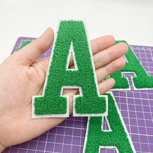 May include: Three green felt letter patches with white outlines. The letters are A, A, and A.