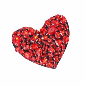May include: A red heart-shaped patch made of rhinestones. The rhinestones are various sizes and shapes, and they are arranged in a random pattern.