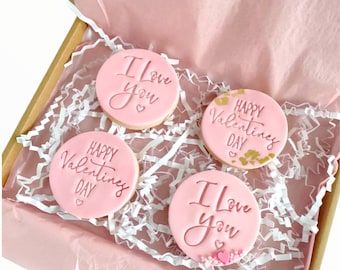 May include: Four pink Valentine's Day cookies in a box. Two cookies say "I love you" and two cookies say "Happy Valentine's Day".