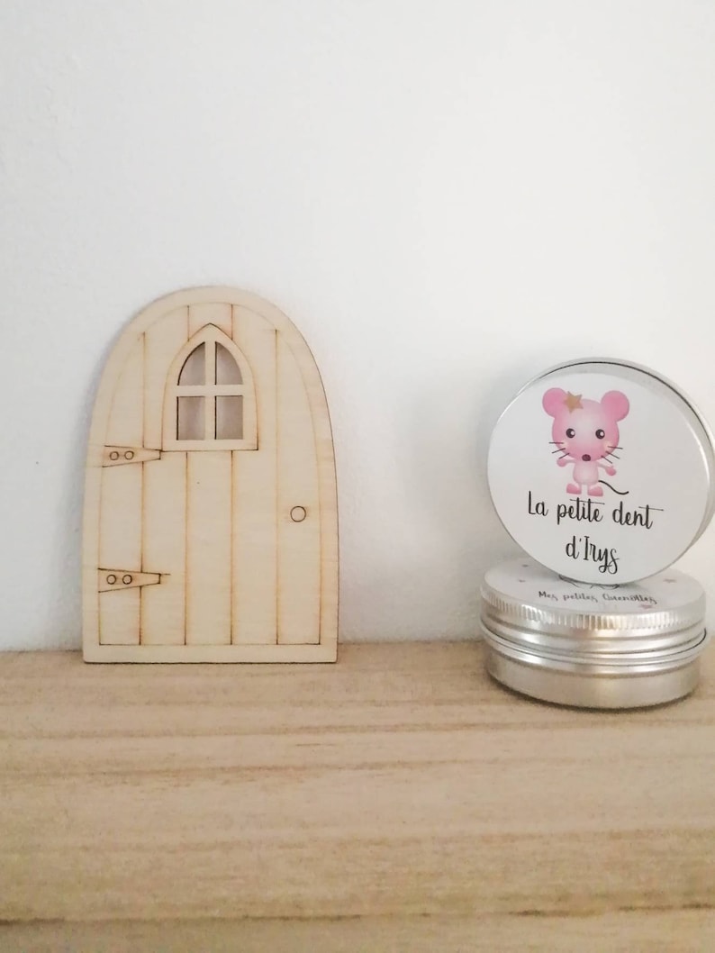 May include: A wooden fairy door with a small window and a silver tin with a pink mouse illustration and the text "La petite dent d'Ilys".