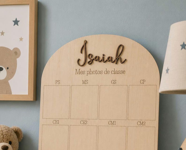 May include: A wooden photo display board with the name "Isaiah" in a cursive font. The board has spaces for school photos labeled PS, MS, GS, CP, CE1, CE2, CM1, and CM2. A framed bear illustration and a lamp with star cutouts are in the background.