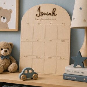 May include: Wooden photo display board with the name "Isaiah" and the text "Mes photos de classe". The board has spaces for school photos and is decorated with a teddy bear, a toy car, and a star-shaped lamp.