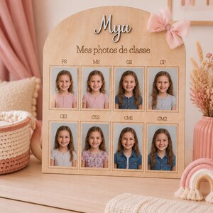 May include: Wooden photo display with the name "Mya" and the text "Mes photos de classe". It features eight school photos of a young girl. A pink bow is attached to the top right corner.