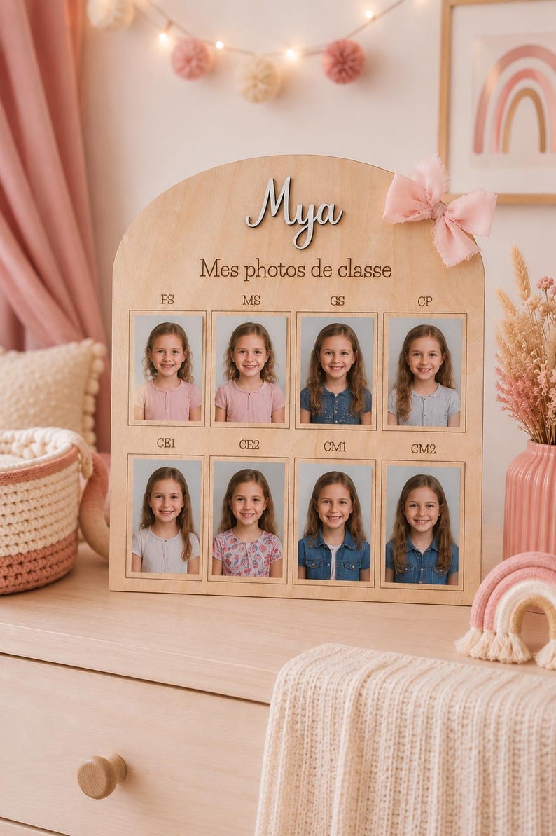 May include: Wooden photo display with the name "Mya" and the text "Mes photos de classe". It features eight school photos of a young girl. A pink bow is attached to the top right corner.