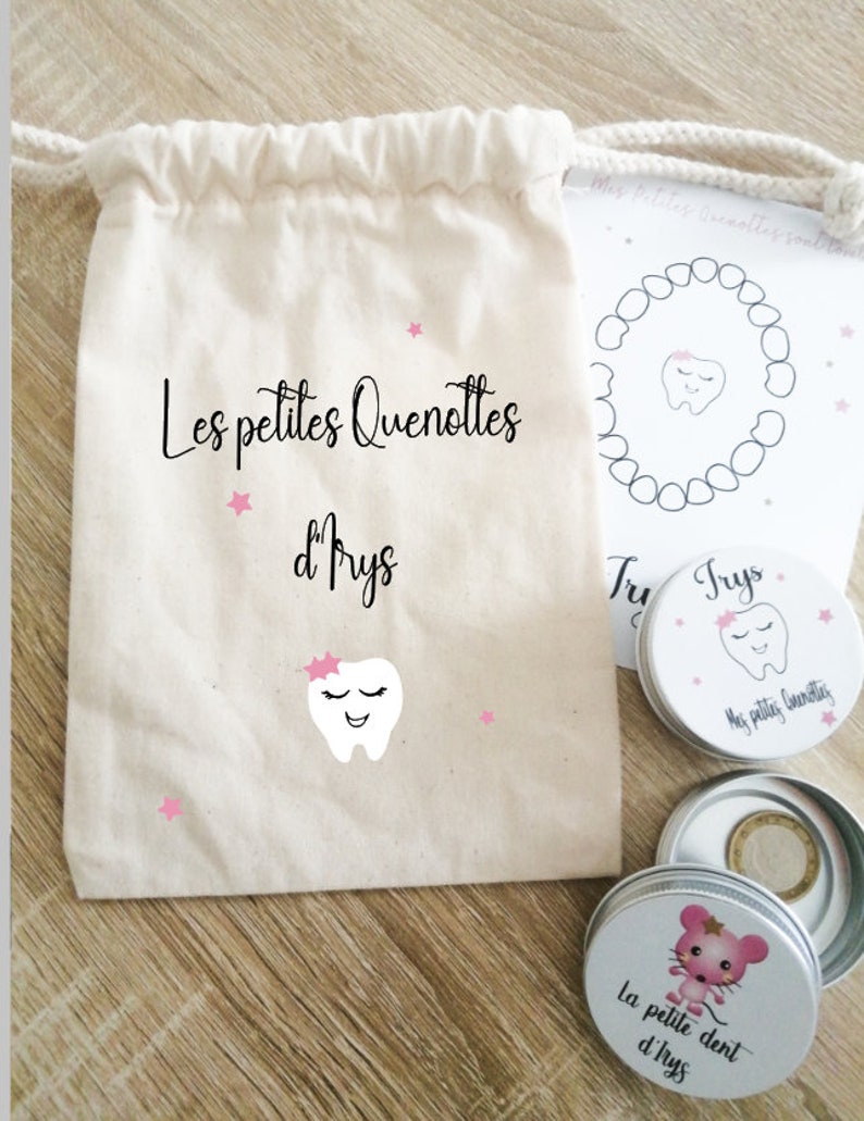 May include: A white cotton drawstring bag with the text "Les petites Quenottes d'Prys" and a pink tooth with a pink bow. There are three small silver tins with pink and white designs. One tin has the text "La petite dent d'lrys" and a pink mouse. Another tin has the text "Trys" and a pink tooth. The third tin has the text "Mes petites Quenottes" and a pink tooth.