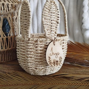 Peut inclure: Un panier en osier tressé en forme de lapin avec une étiquette en bois qui dit "Jays" et un motif floral.