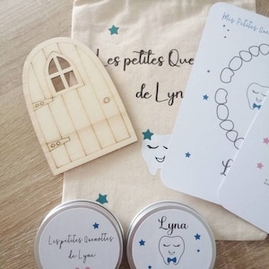 May include: Two small silver tins with white labels. The labels feature blue stars and a cartoon tooth with a bow tie. The text on the labels reads "Les petites Quenottes de Lyna" and "Mes petites Quenottes".