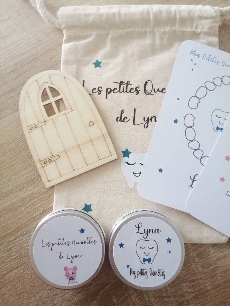May include: Two small silver tins with white labels. The labels feature blue stars and a cartoon tooth with a bow tie. The text on the labels reads "Les petites Quenottes de Lyna" and "Mes petites Quenottes".