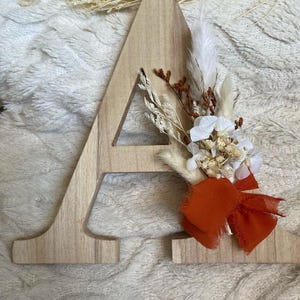 Letra de madera con flores secas y cinta de muselina.