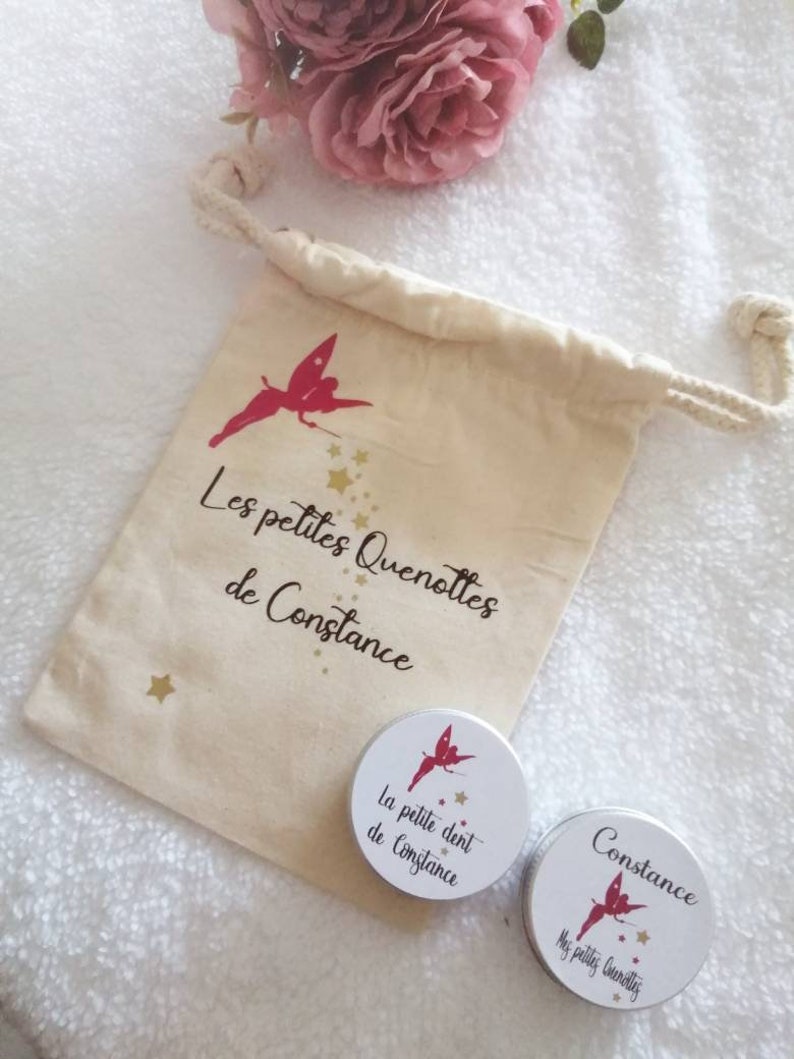 May include: A white drawstring bag with a red fairy and the text "Les petites Quenottes de Constance". Two small round metal containers with red fairies and the text "La petite dent de Constance" and "Constance Mes petites Quenottes".