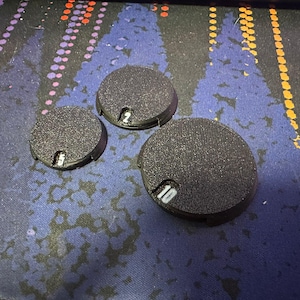 May include: Three black round plastic bases with white numbers 2, 5, and 10 printed on them.