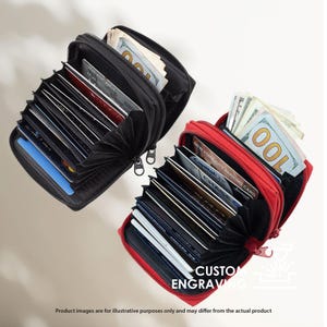 May include: Two zippered wallets, one black and one red, are open to display credit cards and cash. The black wallet is filled with cards and a wad of bills. The red wallet also holds cards and a stack of $100 bills. The text "CUSTOM ENGRAVING" is visible.
